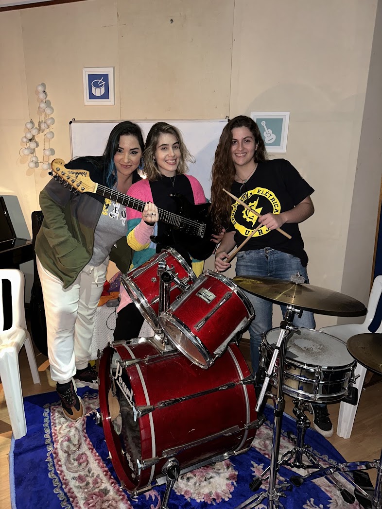 Três alunas com guitarra elétrica e bateria vermelha na sala de música