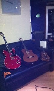 Guitarra semi-acústica vermelha, violão e cavaquinho sobre o sofá